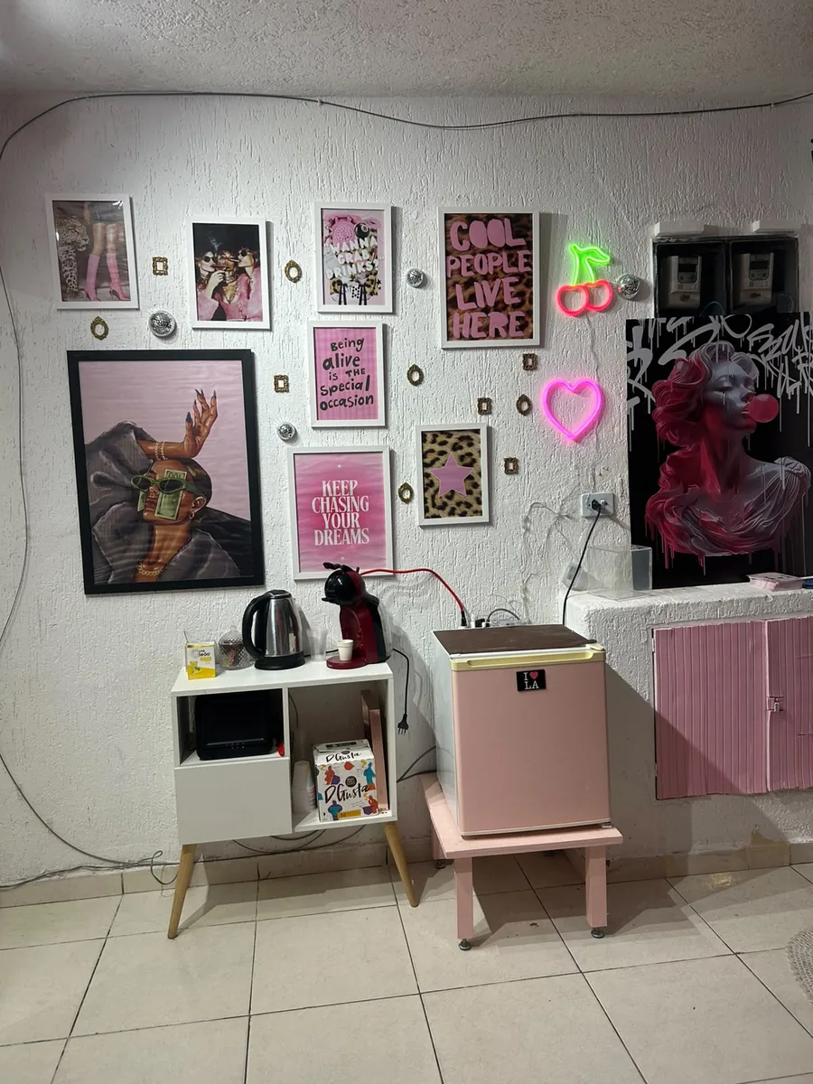 Recepção do studio com parede de quadros em tons de rosa, letreiros de neon e cantinho do café