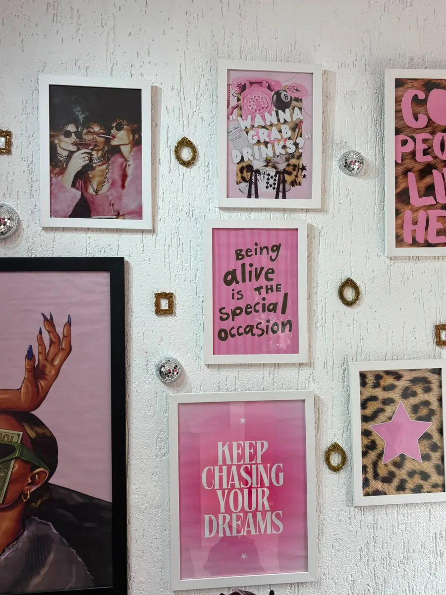 Parede decorativa do studio com quadros e pôsteres em molduras brancas e detalhes em rosa